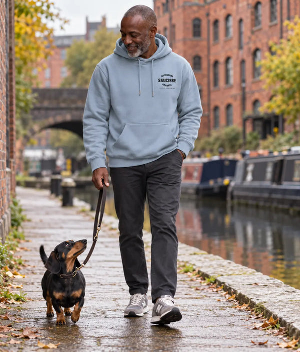 Dachshund owner wearing the Aquamarine Saucisse Manchester England hoodie on a canal walk with a black-and-tan dachshund.