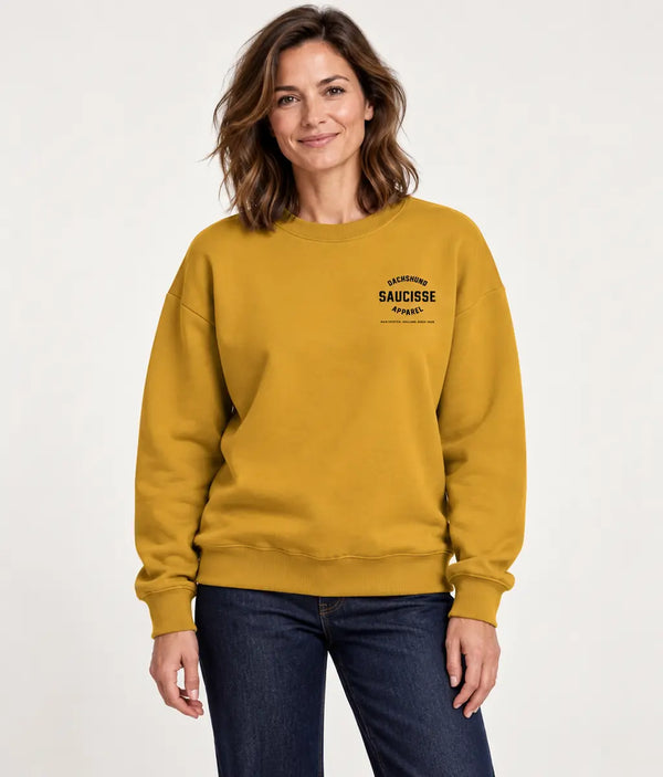 Woman modelling the Saucisse Manchester England unisex sweater in Curcuma against a white studio background