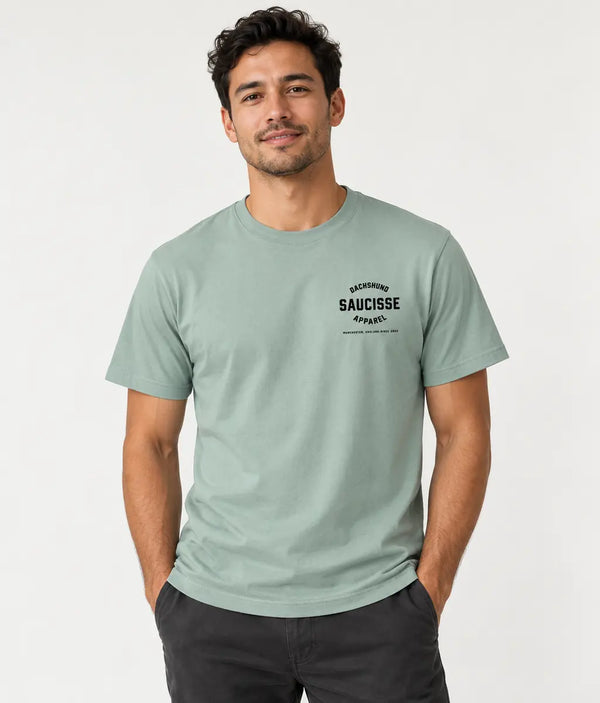 Studio view of a male model wearing the Saucisse Dachshund Apparel Manchester England T-shirt in Aloe