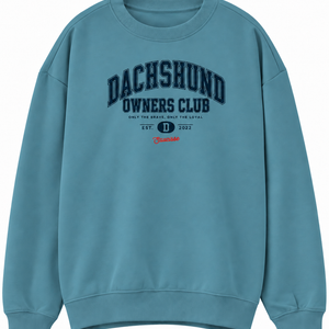 Front of the Saucisse Dachshund Owners Club 2026 unisex sweater in Adriatic Blue, with a navy varsity design and red Saucisse signature