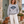 Woman wearing the Saucisse Dachshund Owners Club 2026 unisex sweater in Moon Heather Grey beside a small smooth-haired red dachshund outside a stone cottage