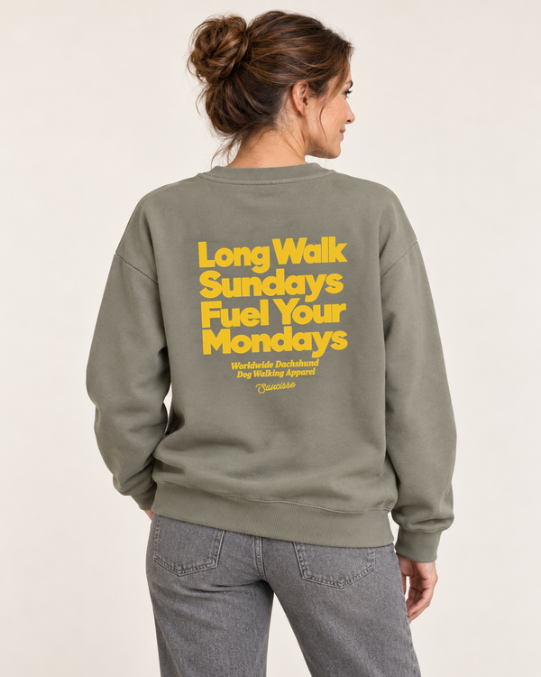 Woman wearing the Saucisse Long Walk Sundays Almond Green sweater in a warm neutral studio, rear view showing the yellow print following the fabric