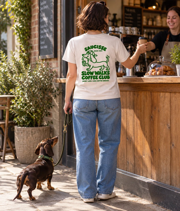 Saucisse Slow Walks Coffee Club unisex T-shirt in Vintage White, rear coffee-stop lifestyle view with green back print and a dachshund on a lead