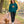 Woman wearing the Saucisse Unzipped long-haired unisex hoodie in Peacock Green while walking a long-haired dachshund beside the water.