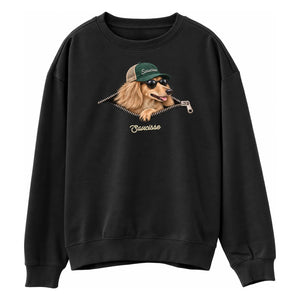 Saucisse Unzipped long-haired unisex sweater in Black, front view showing a long-haired dachshund in a green cap and sunglasses emerging from a printed zip.