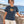 Woman wearing the Saucisse Unzipped long-haired unisex T-shirt in India Ink Grey beside the coast.