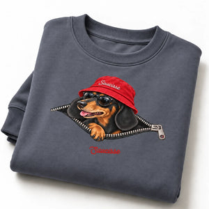 Folded Mineral Grey Saucisse Unzipped Short Haired unisex sweater on a white studio background, showing a dachshund in a red Saucisse bucket hat and sunglasses peeping through an illustrated zip and the red signature.