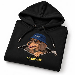 Folded Saucisse Unzipped wire-haired unisex hoodie in Black, showing the dachshund, navy bucket hat and printed zip artwork.