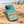 Teal Southwold Sausage Dog Walk 2026 phone case on sand beside British beach huts
