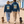 Couple wearing Southwold Sausage Dog Walk 2026 Saucisse hoodie and sweater while walking dachshunds by beach huts