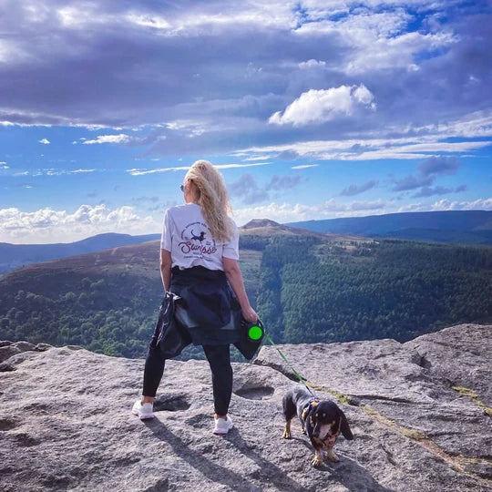 A customer in a white Saucisse T-shirt with a dachshund on a hillside walk
