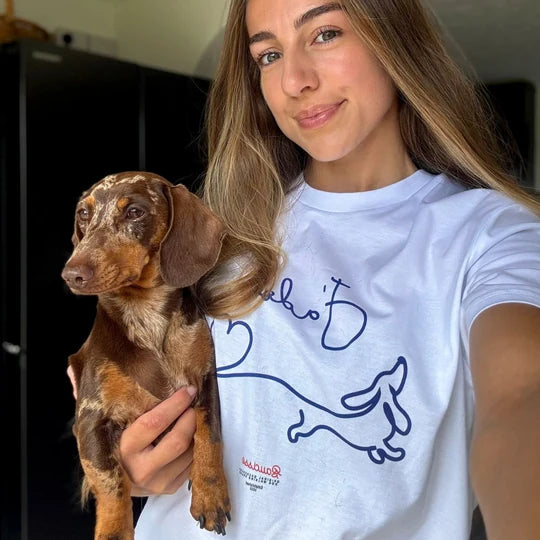 A customer in a white Saucisse T-shirt holding a dachshund