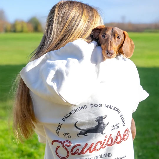 A dachshund looking over a customer’s white Saucisse hoodie on a sunny walk
